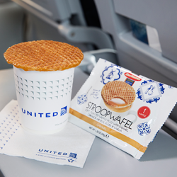 Stroopwafel sitting on cup of illy coffee on a plane seat's tray table.