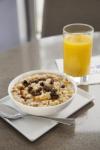Image of a bowl of oatmeal with granola and raisins and a glass of orange juice