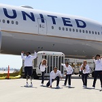 Five Olympic athletes posing in front of a United plane