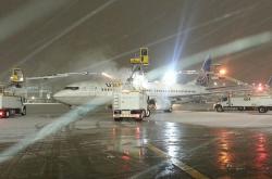 United airpline getting de-iced on tarmac by several de-icing trucks.