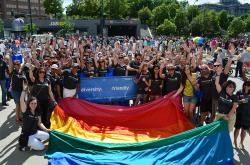 Large group of people, smiling and waving and holding a large rainbow flag