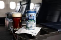 Glass of beer and can of Sam Adams Winter Lager on airplane tray table