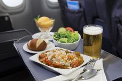 Plate of chicken and sausage jambalaya with dinner roll, glass of beer, and cup of sorbet, served on airplane tray table.