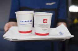 Flight attendant holding tray of paper cups with illy and United branding.